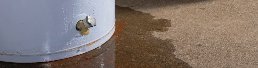Leaking water heater with puddle on the floor.