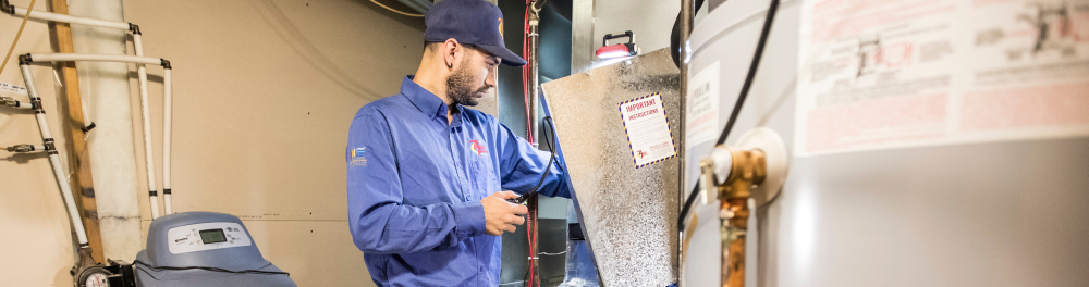 An Action Furnace technician carefully inspects the interior components of a residential furnace.